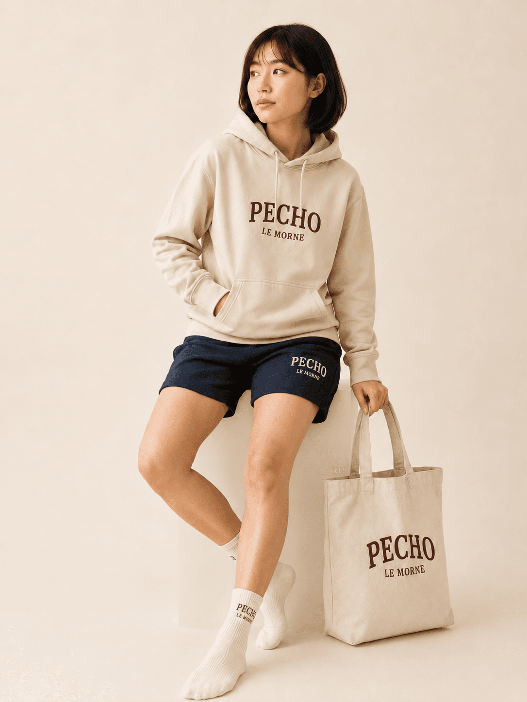 Modèle assise portant un hoodie Le Morne écru, tenant un tote en toile